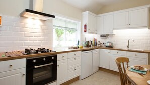 A kitchen with white cabinets, a stove, a dishwasher, and a window with a view of greenery. - 2 Bed in Howden (oc-g0104) (Saltmarshe)