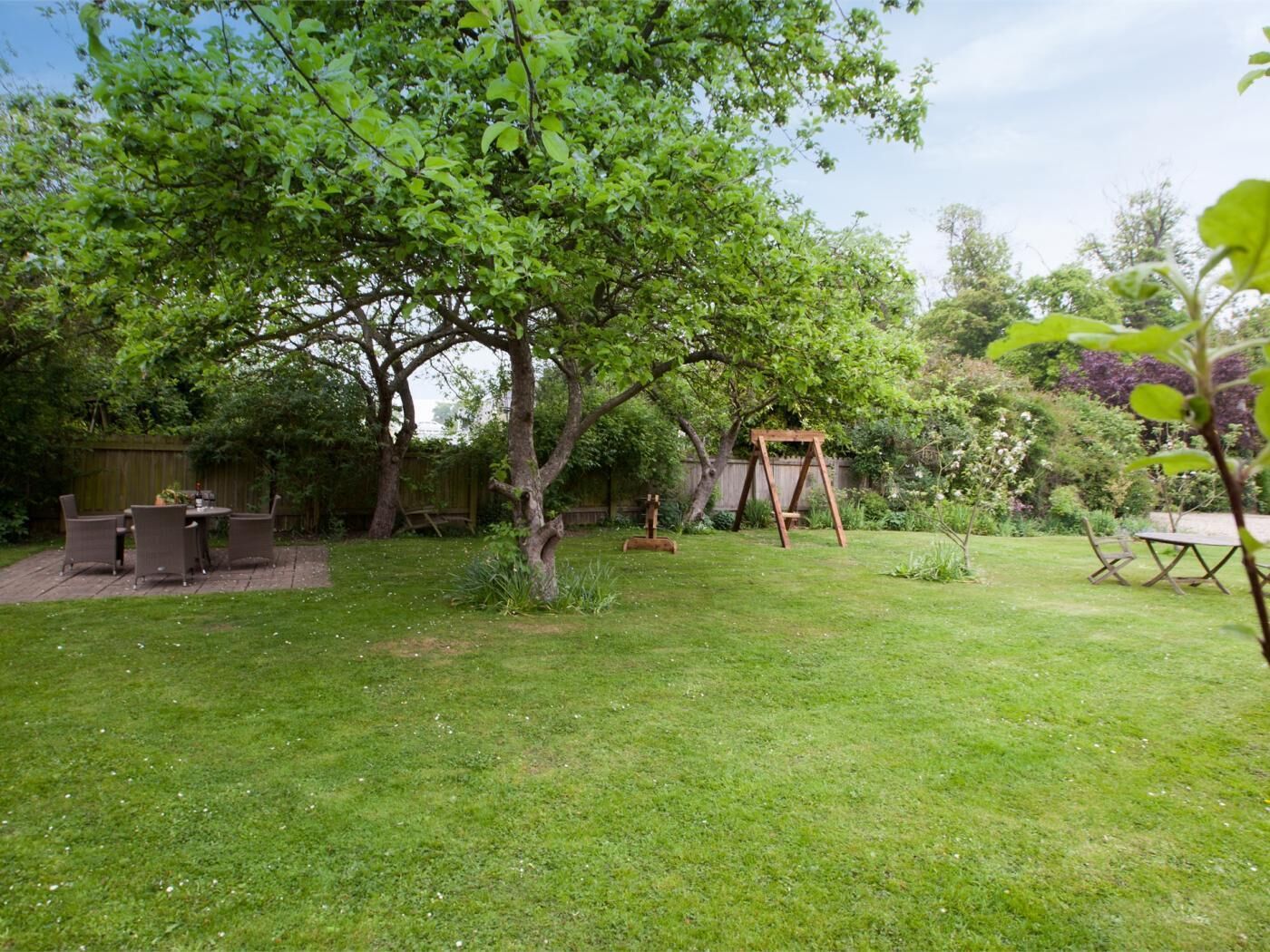 Un jardin avec une balançoire en bois, une table à manger avec des chaises et un petit espace potager.