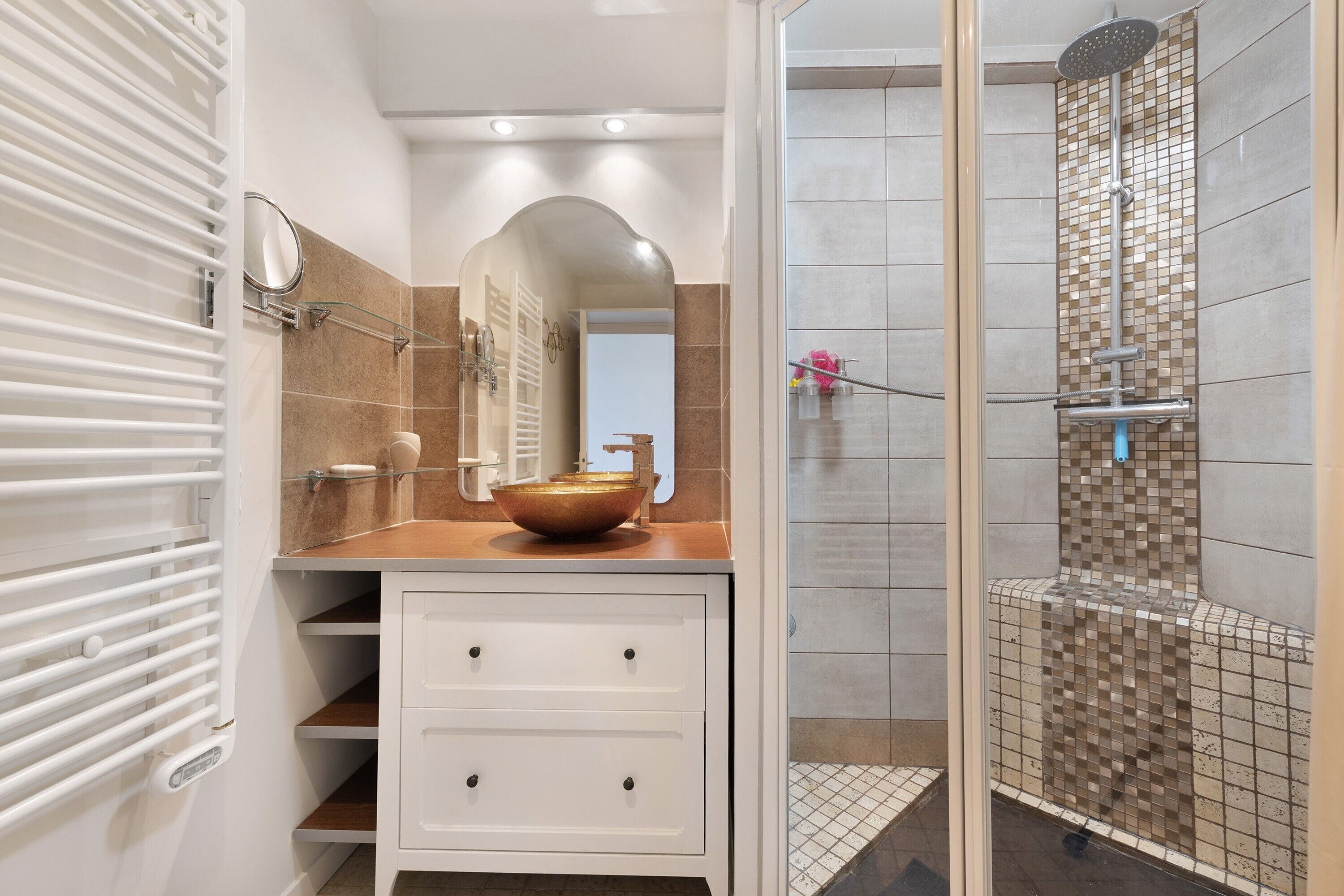 Een moderne badkamer met een wastafel, een grote spiegel, een glazen wasbak en een douche met mozaïektegels.