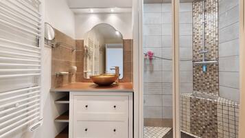 A modern bathroom with a vanity, a large mirror, a glass bowl sink, and a shower with mosaic tiles.