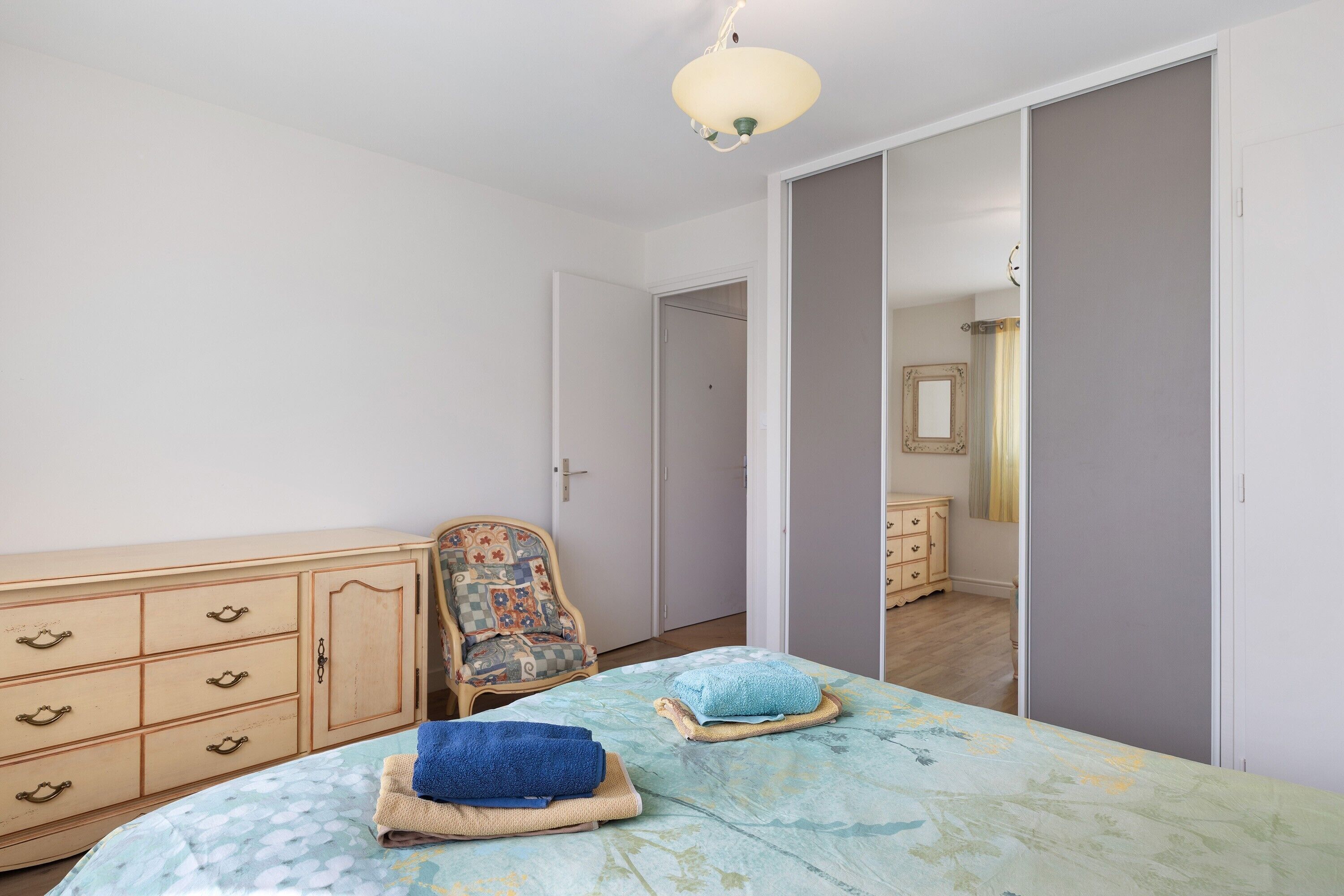 A bedroom with a bed, a chair, a wardrobe, and a mirror.
