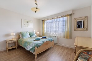 Een slaapkamer met een bed, nachtkastjes, een lamp, een raam met gordijnen, een spiegel en een schilderij aan de muur.