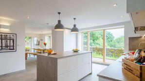 A modern kitchen with a central island, pendant lighting, and large windows offering a view of greenery. - 3 Bed in Matterdale (oc-83002) (Ullswater)