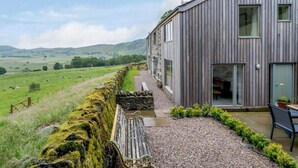 A rustic wooden building with a stone wall, a bench, and a table with chairs. - 3 Bed in Matterdale (oc-83002) (Ullswater)