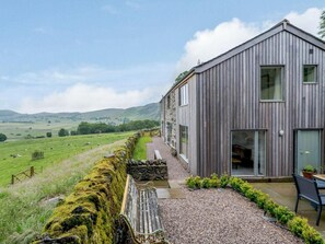 A rustic wooden building with a stone wall, a bench, and a table with chairs. - 3 Bed in Matterdale (oc-83002) (Ullswater)