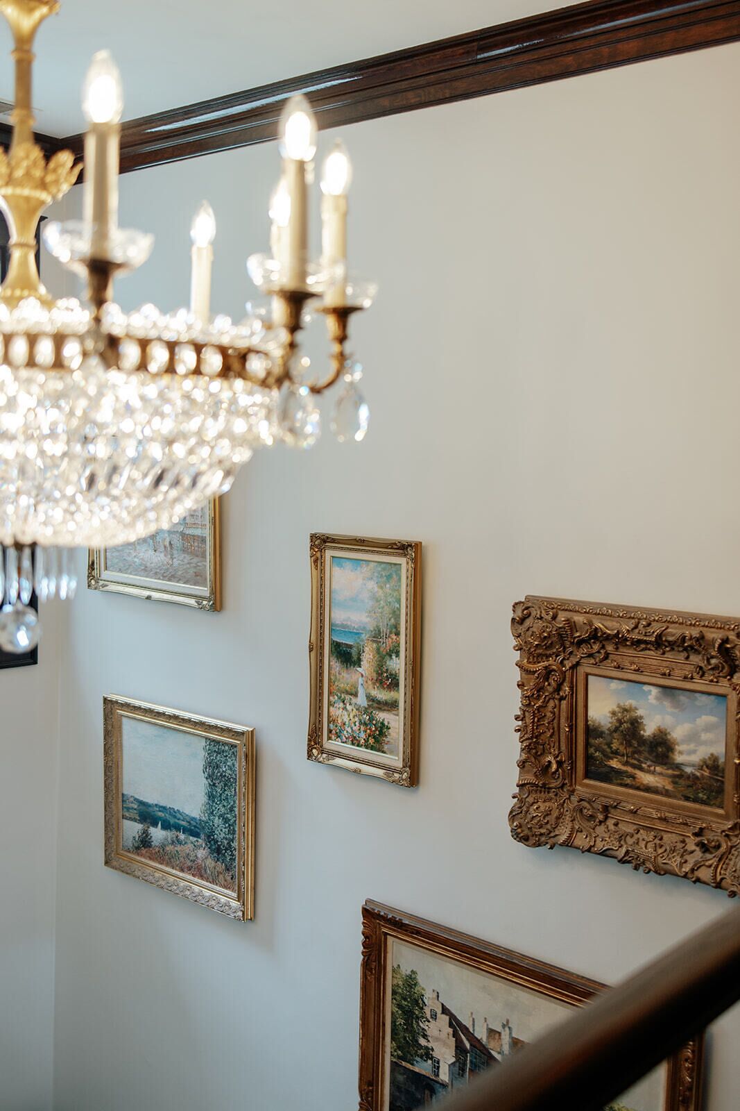 A chandelier, three framed paintings, and a wooden staircase.