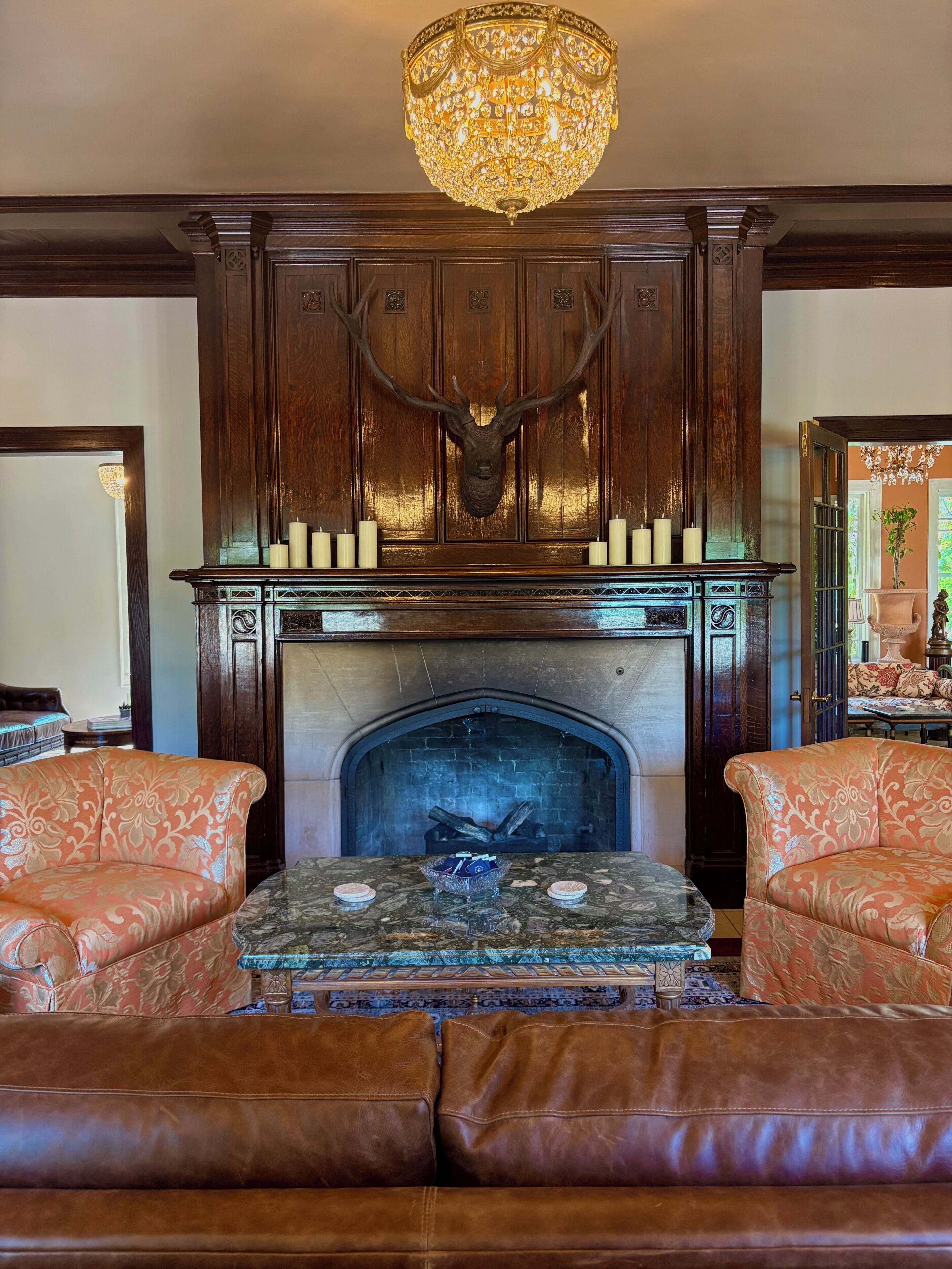 A fireplace with a deer head, surrounded by ornate wood paneling and a chandelier.
