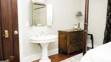 A bedroom with a wooden door, a white pedestal sink, a dresser, and a bed.