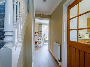 A hallway with a staircase, a dining area with a table and chairs, and a kitchen visible through a window. - 2 Bed in Sheringham (oc-83766) (Sheringham)