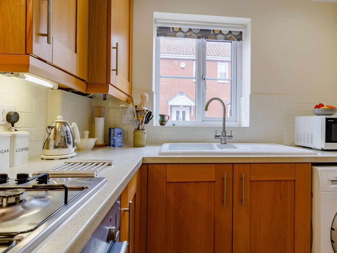 A kitchen with wooden cabinets, a white countertop, a stainless steel stove, a microwave, and a window with a view of a building.
