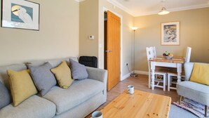 Ein Wohnzimmer mit grauem Sofa, einem Holztisch, einem Esstisch mit Stühlen und Kunstwerken an den Wänden.