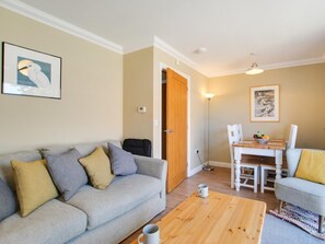 A living room with a grey sofa, a wooden coffee table, a dining table with chairs, and artwork on the walls. - 2 Bed in Sheringham (oc-83766) (Sheringham)