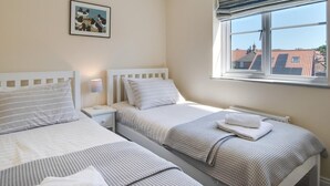 Ein Hotelzimmer mit zwei Betten, einem Fenster mit Blick auf Gebäude, einem Nachttisch mit Lampe und einem gerahmten Bild an der Wand.