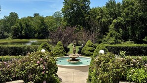 Ein formeller Garten mit einem zentralen Brunnen, geschnittenen Hecken und verschiedenen Bäumen.