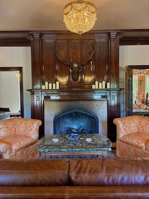 A fireplace with a deer head, surrounded by ornate wood paneling and a chandelier.
