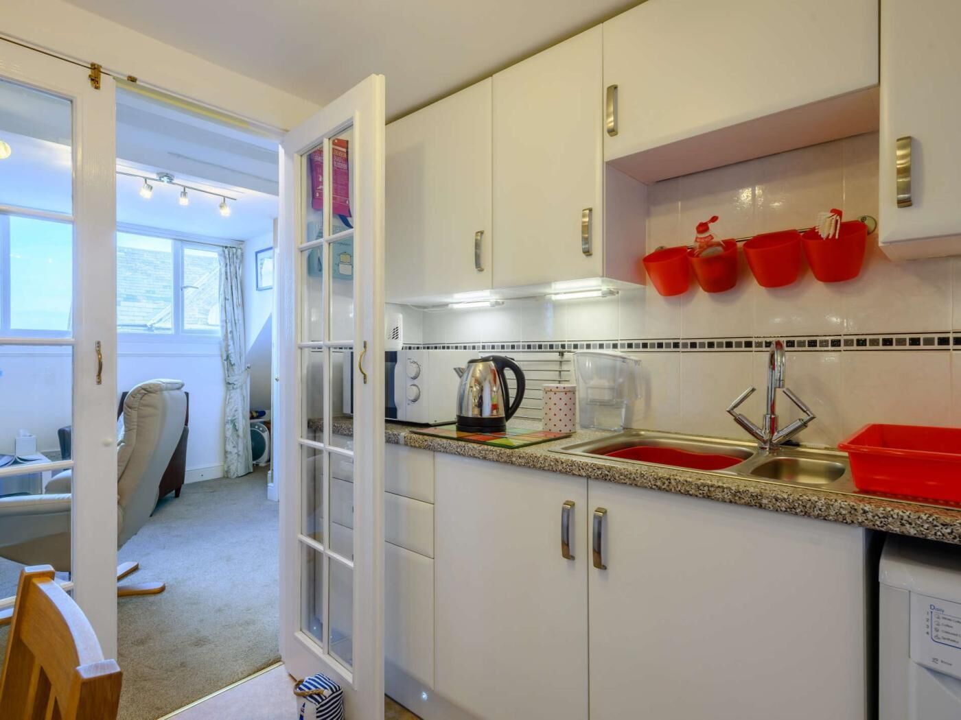 A compact kitchen with white cabinets, a red sink, and a window with curtains.