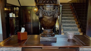 A grand room with a large ornate urn on a wooden table, a staircase with patterned carpet, and a chandelier.