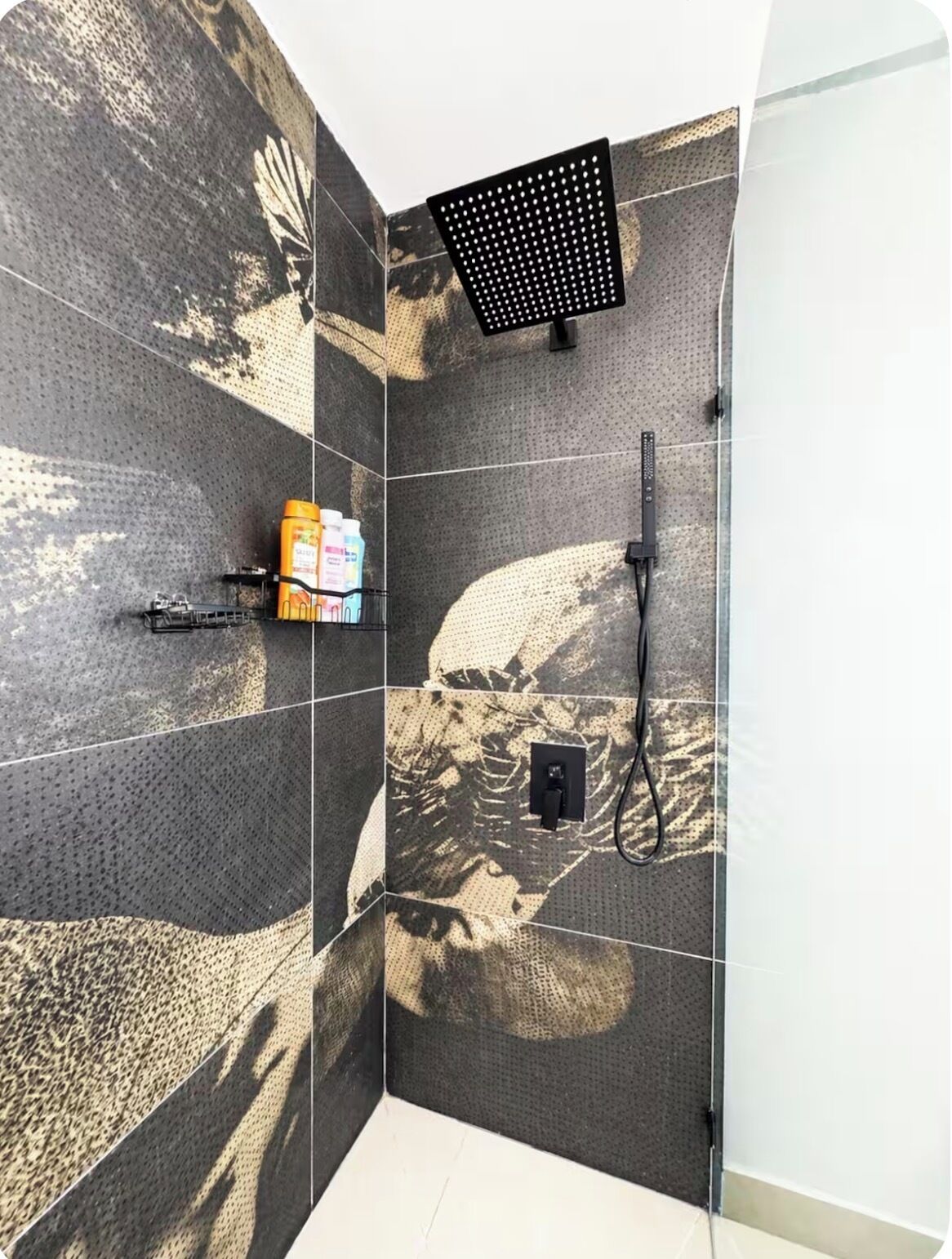 A shower area with a perforated ceiling, a handheld showerhead, and a wall-mounted control panel.