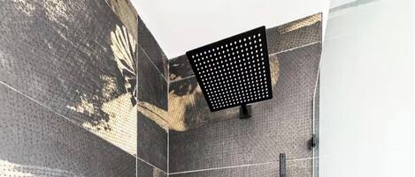 A shower area with a perforated ceiling, a handheld showerhead, and a wall-mounted control panel.