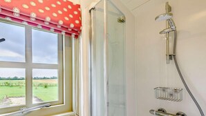 A bathroom with a shower, a window with a red polka dot curtain, and a view of a green field. - 1 Bed in Market Rasen (oc-83846) (Faldingworth)