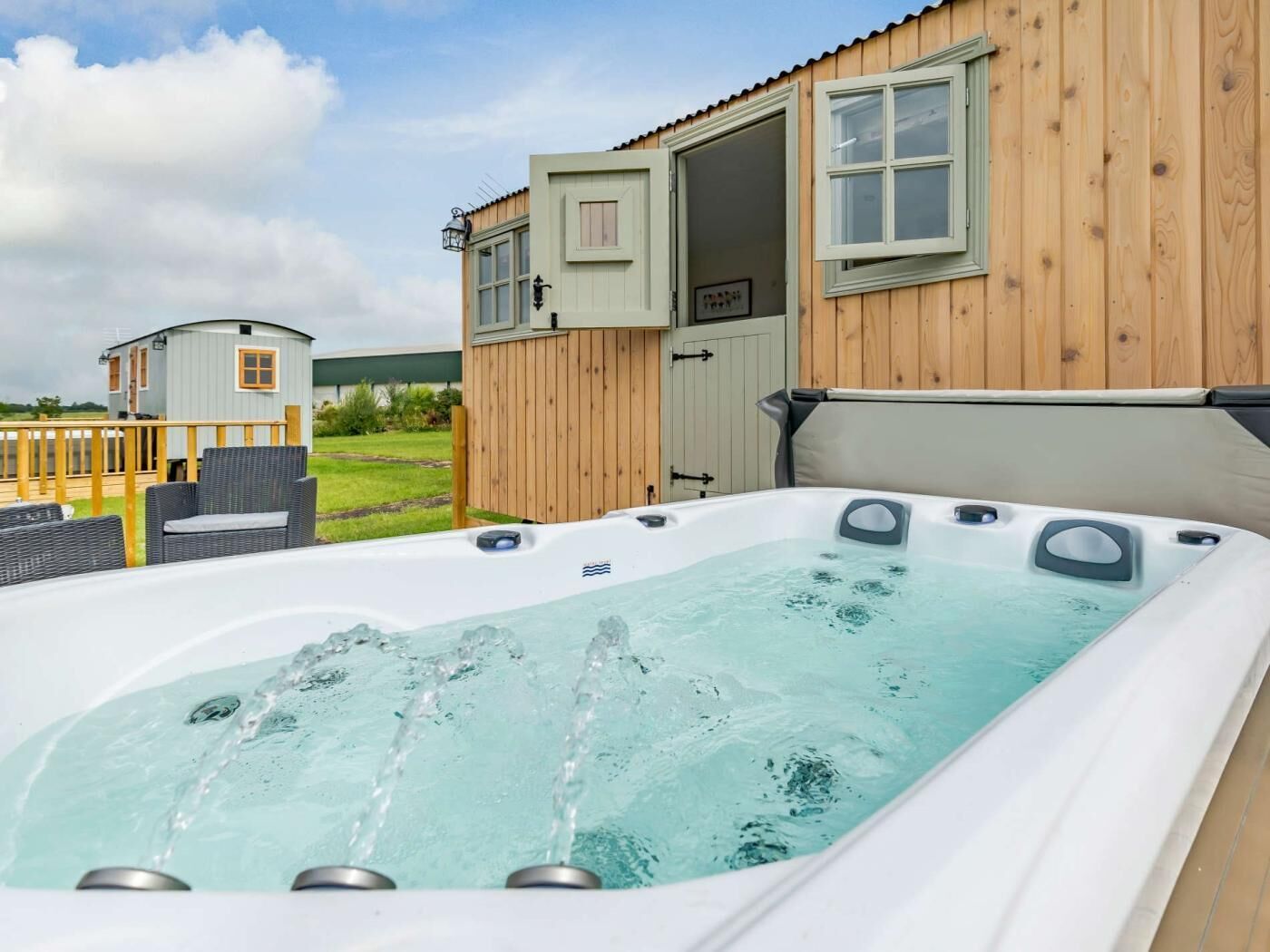 A hot tub with water jets, a wooden deck, and a small building with a door open.