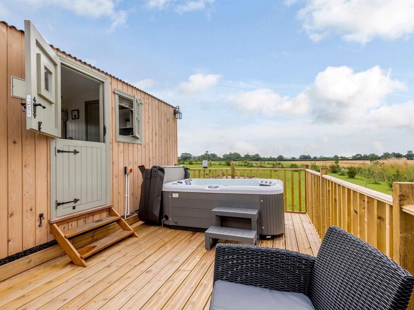 Eine Holzterrasse mit Whirlpool, überdachter Sitzgelegenheit und Blick auf die Landschaft.