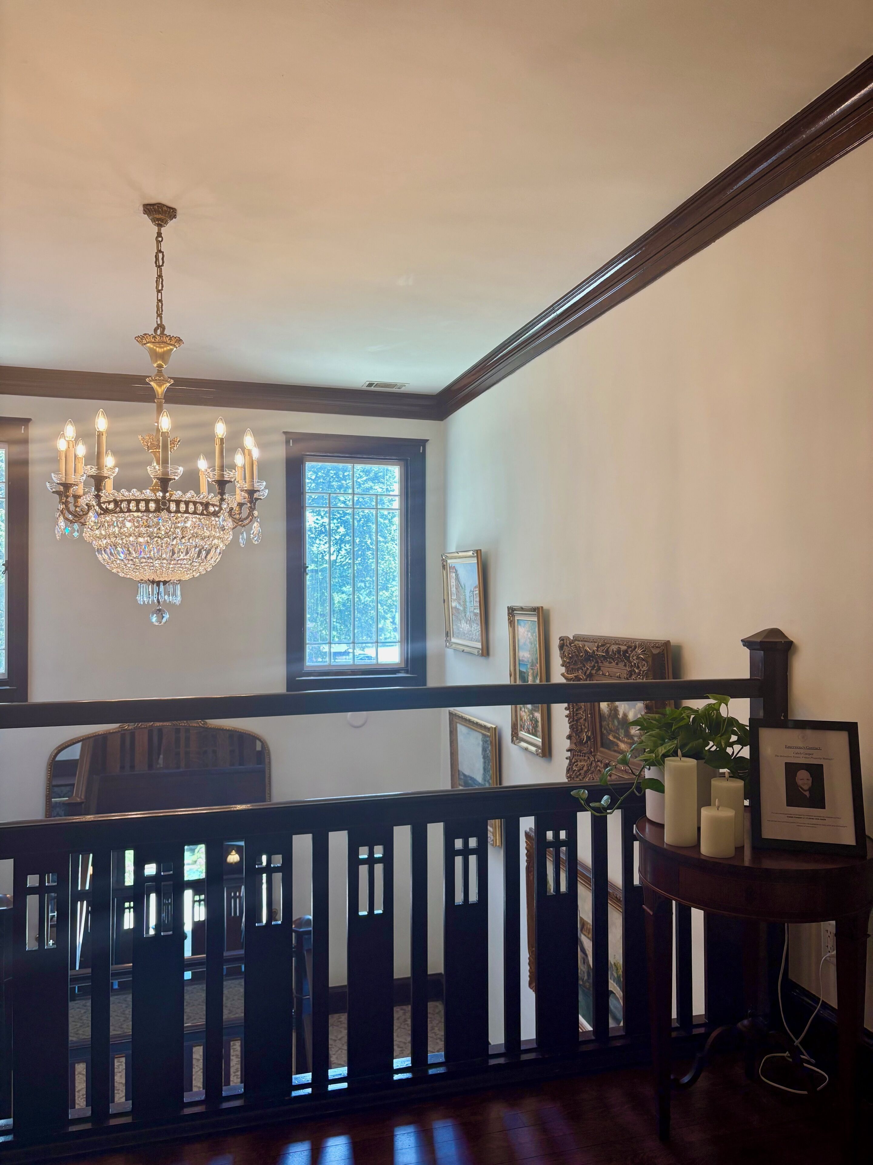 A room with a chandelier, framed pictures, and a window with a view.