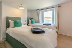 A hotel room with two beds, a window with curtains, a lamp, and a view of the sea. - 3 Bed in Polruan (oc-83821) (Fowey)