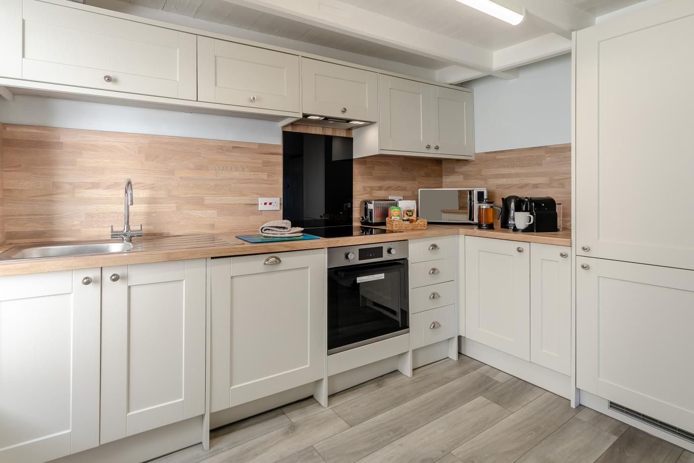 Une cuisine moderne avec des meubles blancs, un plan de travail en bois, un four encastré et un four à micro-ondes.