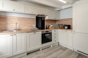 A modern kitchen with white cabinets, a wooden countertop, a built-in oven, and a microwave. - 3 Bed in Polruan (oc-83821) (Fowey)