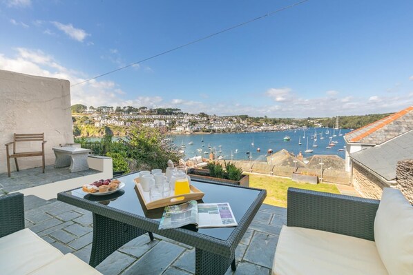 A terrace with a table set for breakfast, overlooking a harbor with boats and a coastal town. - 3 Bed in Polruan (oc-83821) (Fowey)
