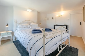 Ein Schlafzimmer mit einem Metallbettgestell, einem Nachttisch mit einer Lampe, einem kleinen zusätzlichen Nachttisch und einer Wandleuchte.