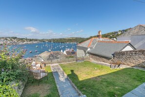 A coastal town with a marina filled with boats, stone buildings, and a grassy area with a pathway. - 3 Bed in Polruan (oc-83821) (Fowey)