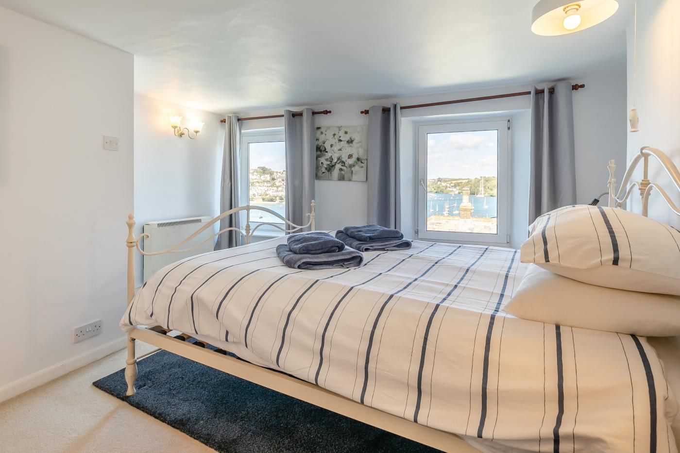 Ett sovrum med en säng, två fönster, utsikt över havet och en taklampa.