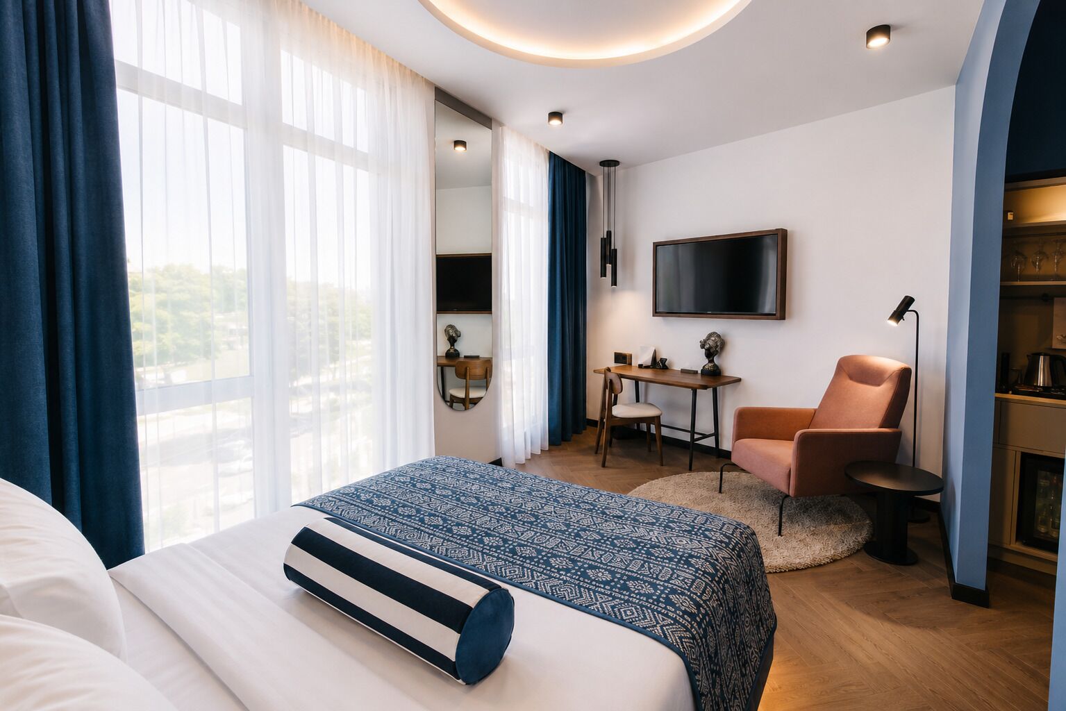 Ein Hotelzimmer mit Bett, Schreibtisch, Stuhl, Fernseher und einer Küchenzeile.