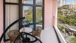 A balcony with a table and chairs, large windows, and a view of buildings and greenery.