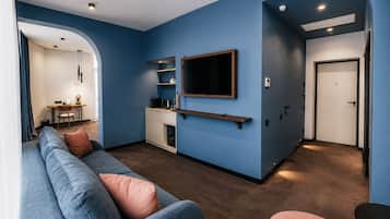 Ein modernes Wohnzimmer mit blauer Akzentwand, einem Wand-Fernseher, einer Couch mit Kissen und einer Küchenzeile mit Arbeitsplatte und Schränken.