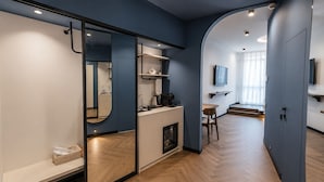 A modern room with a kitchenette, a mirror, a TV, and a wooden floor.