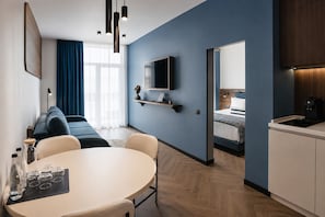 Una habitación de hotel moderna con sofá, una mesa de comedor con vasos, televisión y una zona de cocina.