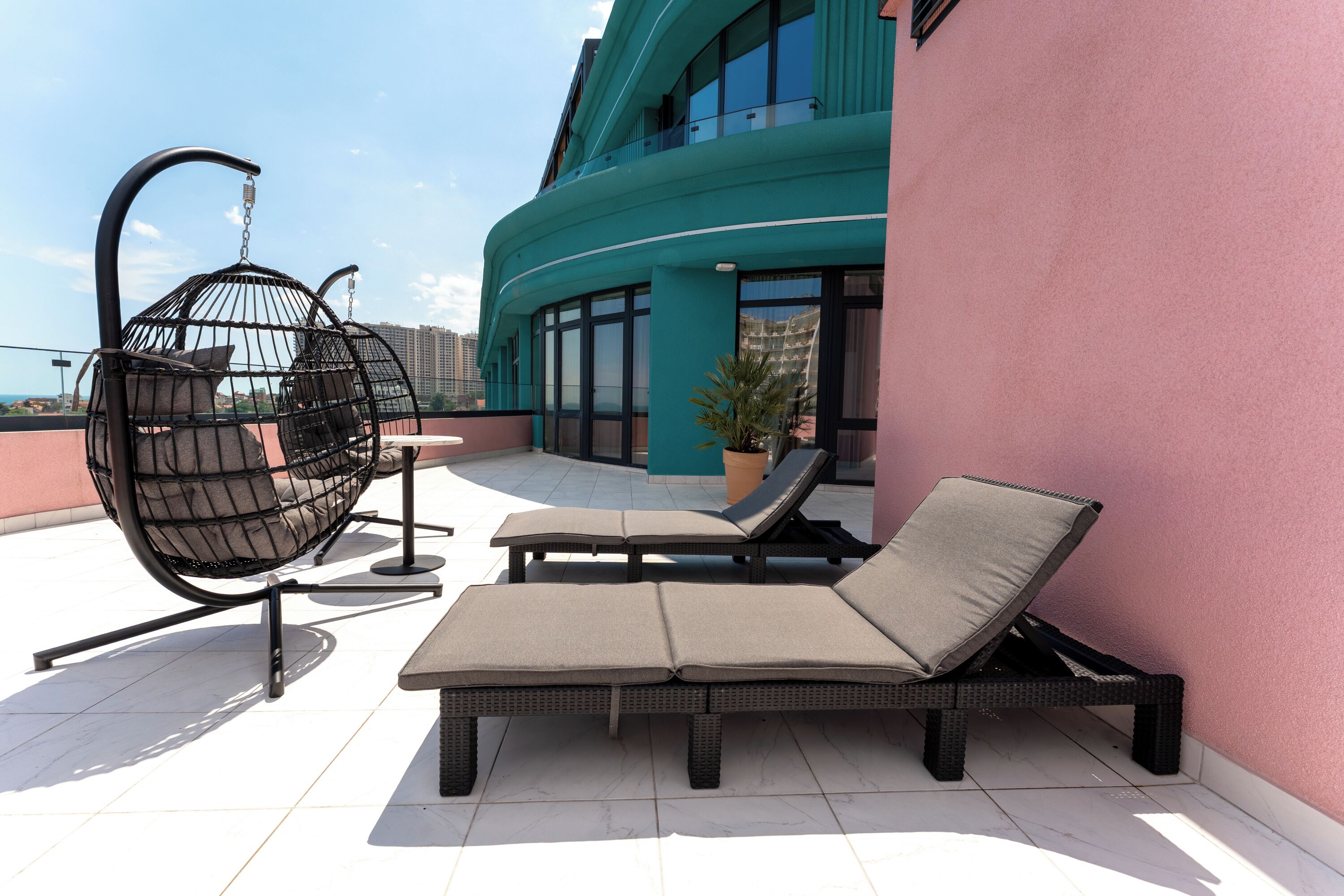 A rooftop terrace with a hanging chair, a lounge chair, and a potted plant.