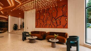 A modern lobby with a geometric light installation, a large abstract wall art, and a seating area with two sofas and two side tables.