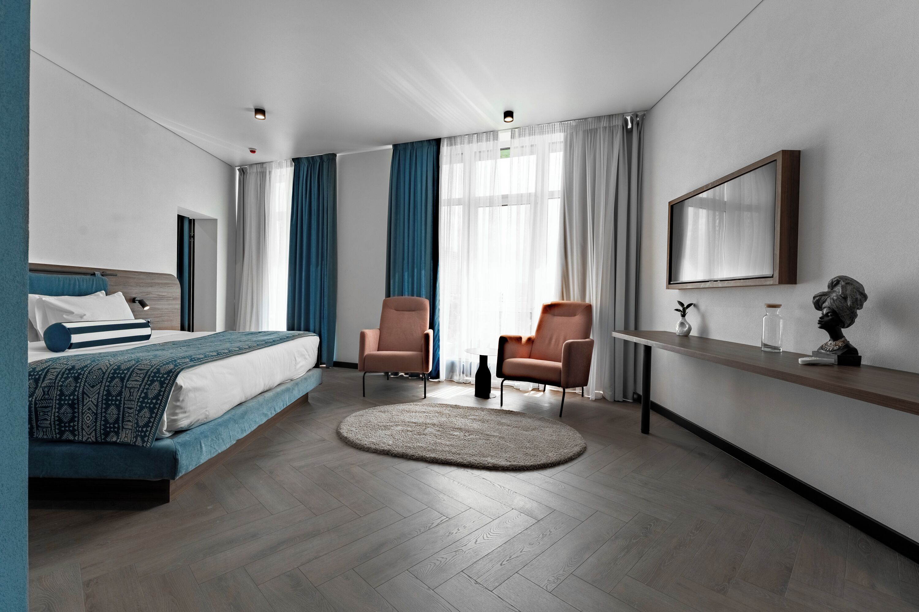 Ein modernes Hotelzimmer mit einem Bett, zwei Stühlen, einem Schreibtisch und einem großen Fenster mit Vorhängen.