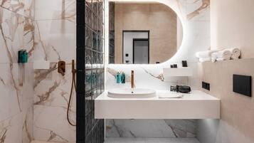 A modern bathroom with a marble wall, a glass shower enclosure, a white sink, and a toilet.