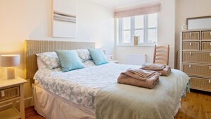 Ein aufgeräumtes Schlafzimmer mit einem Bett, Nachttischen, einer Lampe, einem Fenster und einem Stauraum.