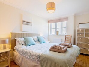 Ein aufgeräumtes Schlafzimmer mit einem Bett, Nachttischen, einer Lampe, einem Fenster und einem Stauraum.