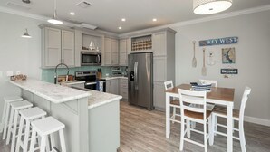 A modern kitchen with a central island, white bar stools, a dining table with chairs, and a 'KEY WEST' sign on the wall. - NAUTICAL NEST - 3-bedroom canal front tranquil home on Summerland Key with AC (Summerland Key)