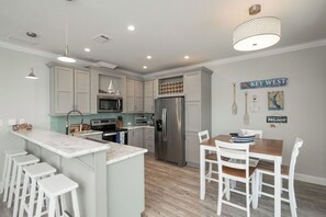 A modern kitchen with a central island, white bar stools, a dining table with chairs, and a 'KEY WEST' sign on the wall. - NAUTICAL NEST - 3-bedroom canal front tranquil home on Summerland Key with AC (Summerland Key)