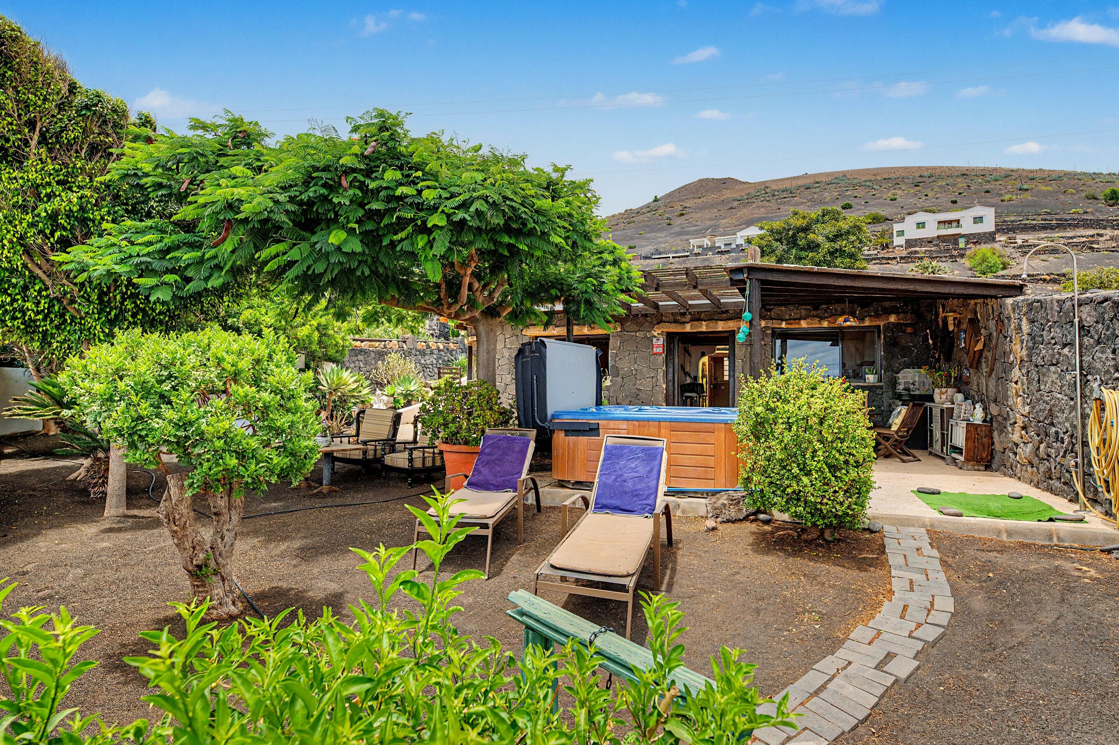 A patio area with lounge chairs, a hot tub, and a stone wall.