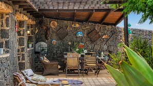 A stone wall with a wooden ceiling, lounge chairs, a table, and chairs.