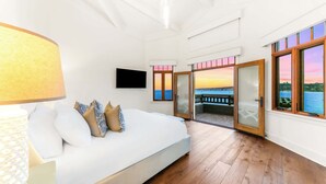Une chambre à coucher avec un lit, des oreillers, une télévision et une vue sur la mer grâce à de grandes fenêtres.